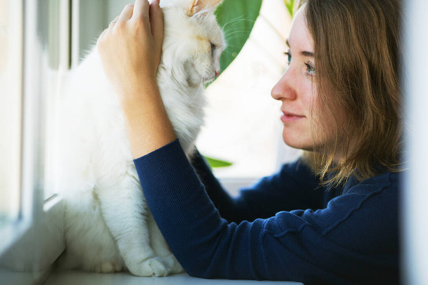 Mujer joven y gato blanco esponjoso amorosamente mirándose entre sí. Cuidado de mascotas y acogedor concepto de hogar - Foto, Imagen