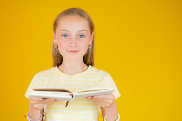 Portret van een mooi meisje dat notities maakt in notitieblok geïsoleerd over gele achtergrond - Foto, afbeelding