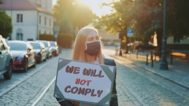 抗議の散歩:人々が遵守していない言葉でプラカードを保持医療マスクの女性 - 映像、動画