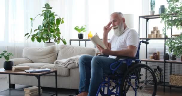 Disabled senior man reading a book sitting on wheelchair - Footage, Video