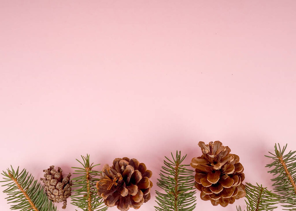 Flat Lay Christmas Background With Ornaments. Top view of pine cones arranged on pink backdrop. - Photo, Image
