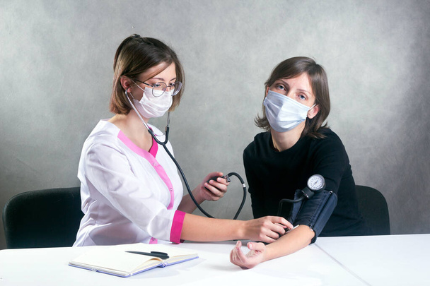 молода жінка-лікар в медичній сукні і маска вимірює кров'яний тиск з тонометром маскованій жінці
 - Фото, зображення