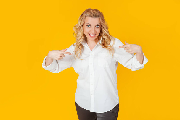 Amazed speechless impressed happy European blonde woman in white shirt pointing at herself shocked, with open mouth, drooping jaw, amazed, to receive an unexpected great offer on a yellow background. - Fotoğraf, Görsel
