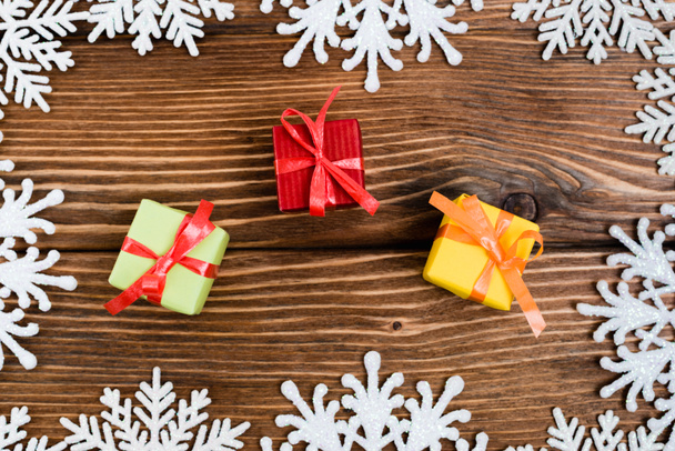 Вид сверху маленьких подарочных коробок возле декоративных снежинок на деревянном фоне, новогодняя концепция - Фото, изображение