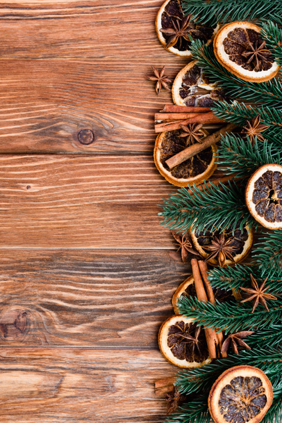 Top view of dry orange slices, anise stars, cinnamon sticks and pine branches on brown wooden background - Foto, afbeelding