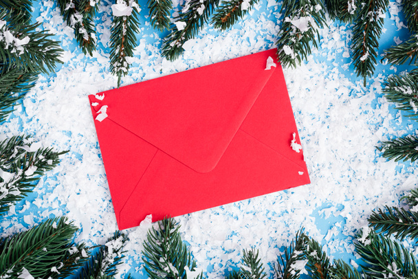 Top view of red envelope, artificial snow and pine branches on blue background, new year concept - Foto, Imagem