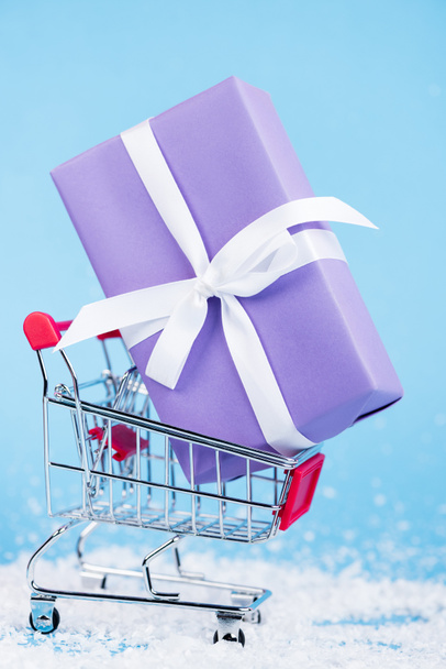 Close up view of little gift in shopping trolley on blue background, new year concept - Photo, Image