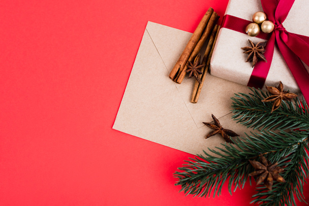Top view of gift with envelope, cinnamon sticks, anise stars and pine branch on red background - Fotografie, Obrázek