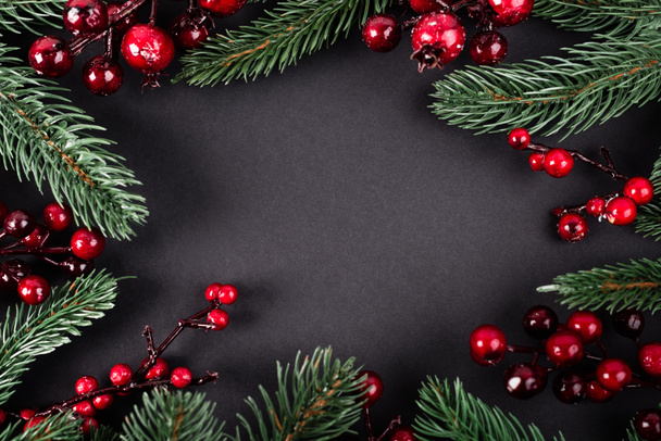 Bovenaanzicht van rode kunstmatige bessen en dennentakken op zwarte achtergrond, nieuwjaarsconcept - Foto, afbeelding