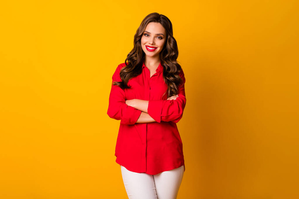 Photo of pretty curly business lady bright pomade bossy person friendly smiling teeth arms crossed wear office red shirt white trousers isolated yellow vivid color background - 写真・画像