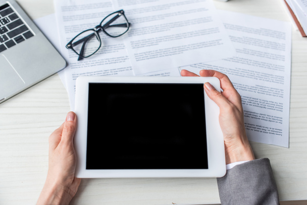 Vista recortada de empresaria sosteniendo tableta digital con pantalla en blanco cerca de documentos y anteojos en el lugar de trabajo - Foto, Imagen