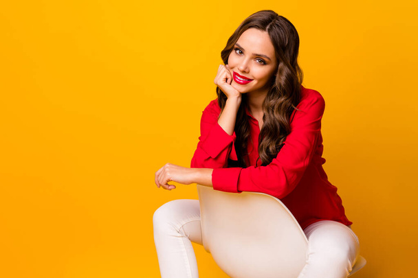 Photo of attractive business lady toothy smiling sit cosy chair between legs lean chin arm cheerful wear red shirt white trousers isolated yellow vivid color background - Foto, Imagen
