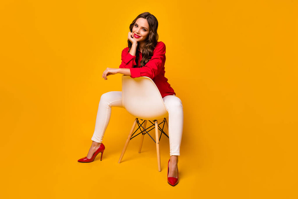 Фотографія повного тіла привабливої ділової леді сидить затишний стілець між ногами нахилена голова руки веселий одяг червона сорочка білі штани на високих підборах ізольовані жовтий яскравий кольоровий фон
 - Фото, зображення