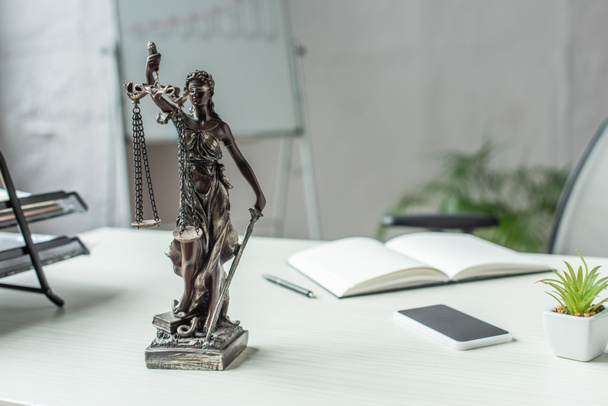 Themis figurine with cellphone and blank notebook on table with blurred flipchart on background - Photo, Image