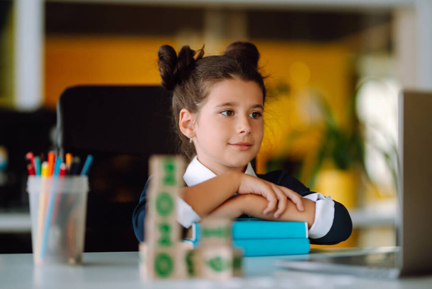 Κομψό κορίτσι του σχολείου κάθεται στο τραπέζι με βιβλία. Αυτοαπομόνωση, διαδικτυακή εκπαίδευση, κατ 'οίκον διδασκαλία. Covid-2019. - Φωτογραφία, εικόνα