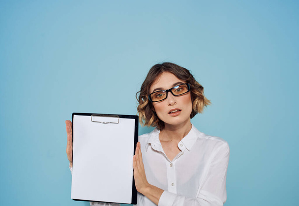 Teczka z białą kartką papieru w rękach kobiet na niebieskim tle i okularami na twarzy - Zdjęcie, obraz