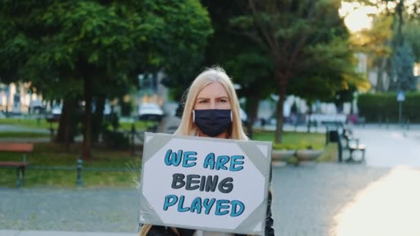 Bella ragazza con la maschera medica che protesta contro le autorità che giocano vite umane - Filmati, video