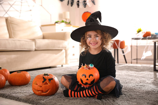 Cute little girl with pumpkin candy bucket wearing Halloween costume at home - Zdjęcie, obraz