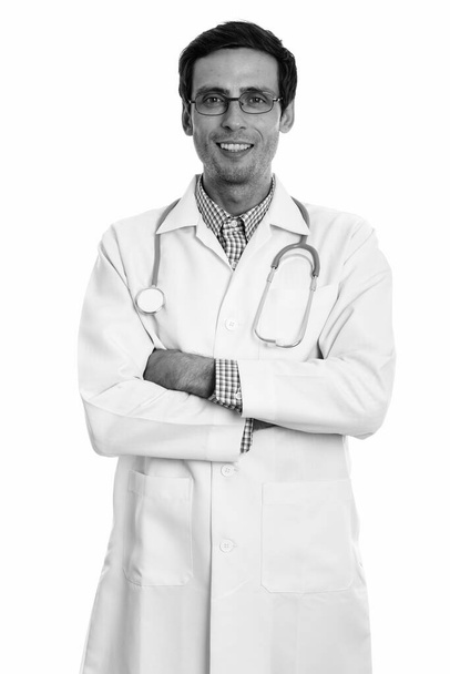 Studio shot of young happy man doctor smiling while wearing eyeglasses with arms crossed - Foto, imagen