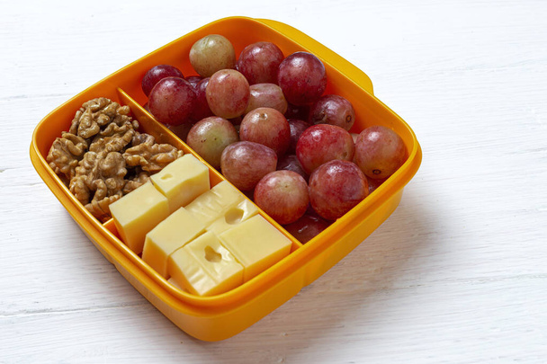 プラスチック容器の健康食品は、作業台の上にチーズ、ブドウ、クルミで食べる準備ができています。To take away.walnuts - 写真・画像
