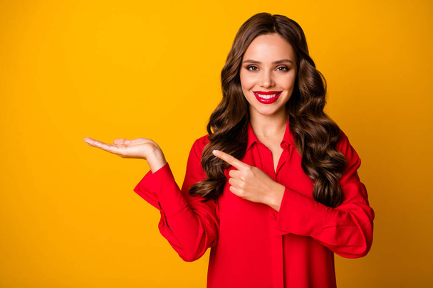 Photo of pretty curly business lady hold open hand empty space sales manager offer novelty product direct finger arm wear red office shirt isolated yellow bright color background - Fotó, kép