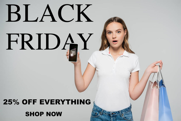 Schockierte Frau mit Smartphone und Einkaufstasche in der Nähe von Black Friday, Shop jetzt Schriftzug auf Grau  - Foto, Bild