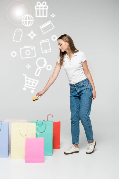young woman holding credit card near shopping bags and illustration on grey, black friday concept - Фото, изображение