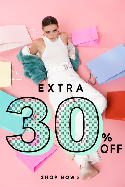 overhead view of young woman in blue faux fur jacket sitting near shopping bags and extra 30 percent off lettering on pink - Φωτογραφία, εικόνα