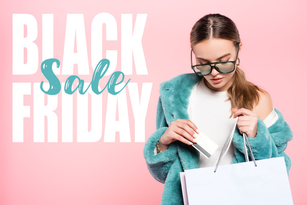 mujer de moda en gafas de sol con tarjeta de crédito cerca de la bolsa de compras y letras de venta de viernes negro en rosa - Foto, Imagen