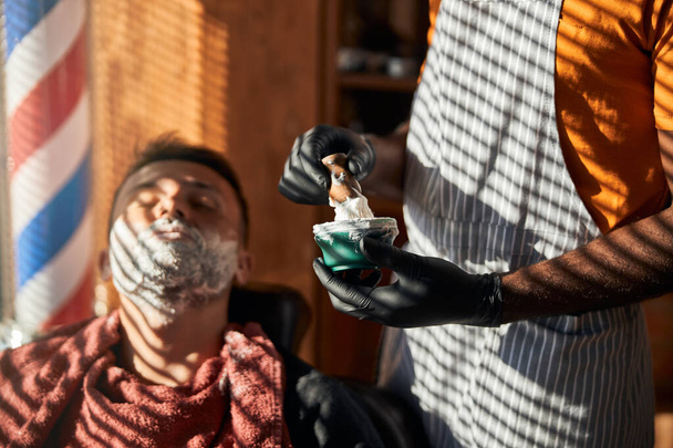 Fryzjer w sterylnych rękawiczkach przygotowujący krem do golenia w salonie fryzjerskim - Zdjęcie, obraz