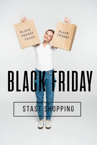 pleased woman with closed eyes holding shopping bags near black friday stast shopping lettering on white - Photo, Image