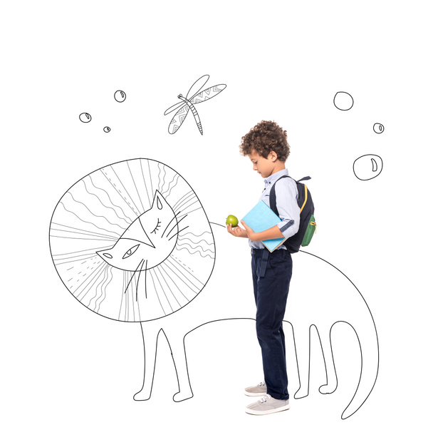 вид сбоку кудрявого школьника с рюкзаком и книгой, держащей яблоко рядом с иллюстрировкой волшебных персонажей на белом фоне  - Фото, изображение