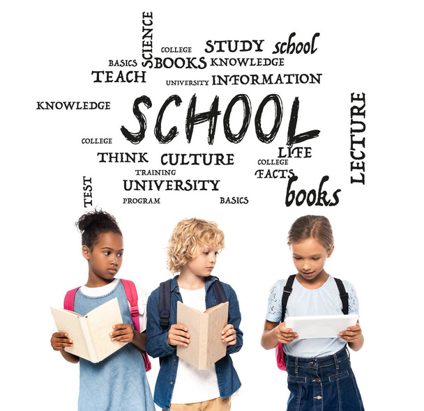 afro-américaine écolière et écolier blonde avec des livres regardant tablette numérique dans les mains de camarade de classe près de lettrage sur blanc  - Photo, image
