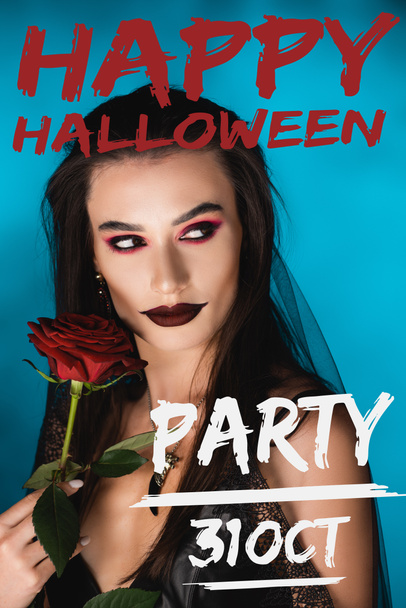 mysterious young woman with black makeup in veil looking away near rose and happy halloween party lettering on blue - Photo, Image