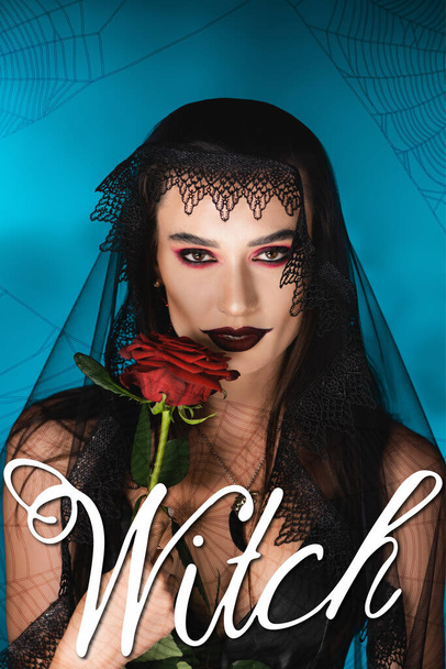evil woman with black makeup and dark veil holding rose near witch lettering on blue - Photo, Image