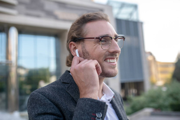 Smiling male office worker wearing wireless earphones outside - Foto, immagini