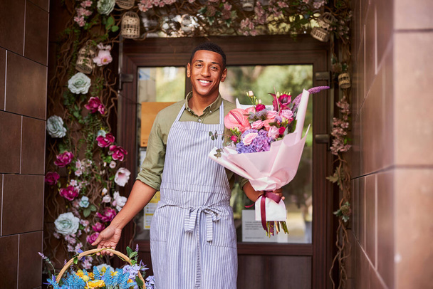 Kind mixed-race worker carrying flowers in both hands - 写真・画像