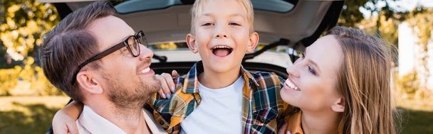 Cheerful son embracing parents near car on blurred background outdoors, banner  - Foto, Imagen