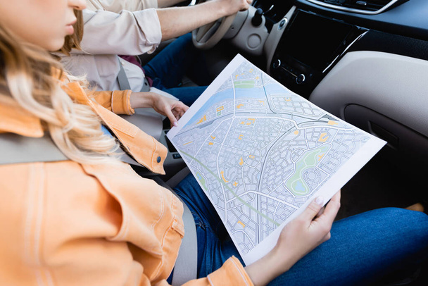 Обрезанный вид женщины, держащей карту рядом с мужем за рулем автомобиля на размытом фоне  - Фото, изображение