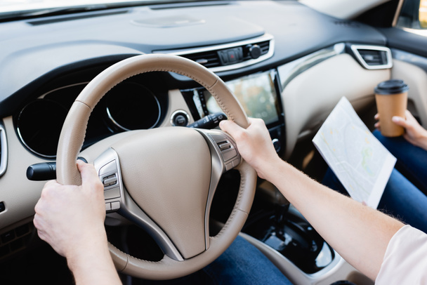 Обрізаний вид людини, що водить машину біля дружини з картою та виймає каву на розмитому тлі
  - Фото, зображення