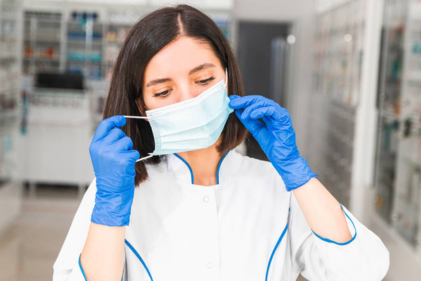 fatigué jeune médecin ou pharmacien d'origine ethnique du Moyen-Orient enlevant masque médical bleu et gants dans le couloir de l'hôpital - Photo, image