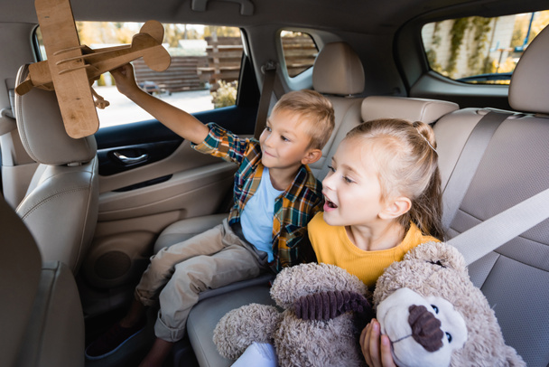 Vrolijke kinderen met speelgoed zitten op de achterbank van auto   - Foto, afbeelding