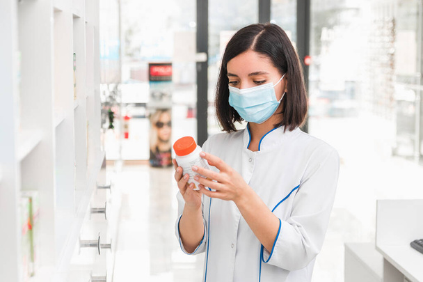 choosing the right medicine. professional looking female pharmacist with medical mask on in drug store studying the prospectus of a new drug - Photo, Image