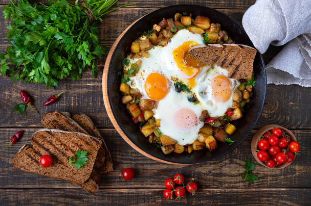 Fried eggs with vegetables  - shakshuka in a frying pan and rye bread on an old wooden background. Late breakfast. Rustic style. Middle eastern traditional dish.  Flat lay. Top view - Photo, Image