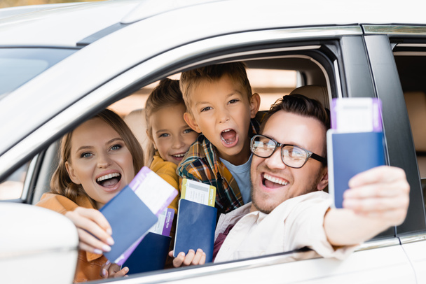 Famiglia allegra con bambini in possesso di passaporti con biglietti aerei in primo piano sfocati in auto  - Foto, immagini