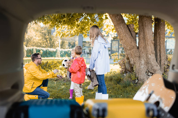 Family in autumn outfit with toys and football standing near trunk of car on blurred foreground  - Photo, Image