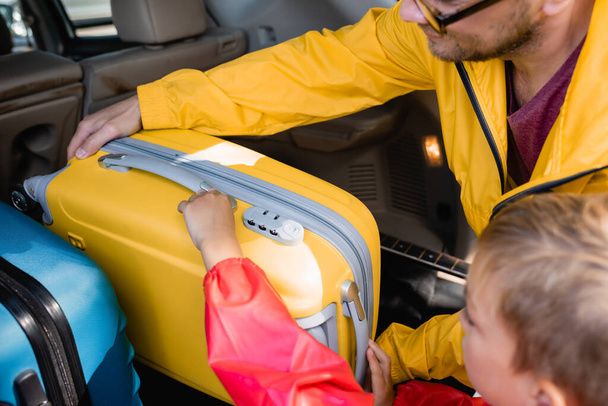Boy and father putting suitcase in trunk of car during trip  - Foto, afbeelding