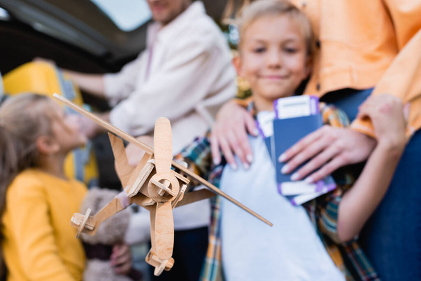 Игрушечный самолет в руке мальчика рядом с семьей с паспортами и машиной на размытом фоне  - Фото, изображение