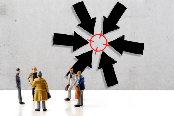 team of people making a decision about their business strategy, five miniature figurines standing in front of concrete wall with hand drawn big arrows with target and thinking about the strategy of how to be successful and how to reach set goals - Photo, Image