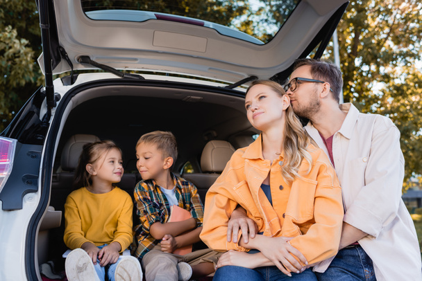 Man hugging wife near smiling kids in trunk of car  - Photo, Image
